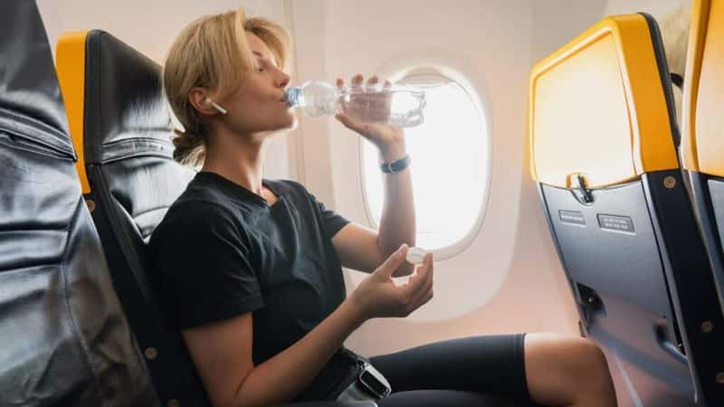 Young woman drinks water during her flight in an airplane