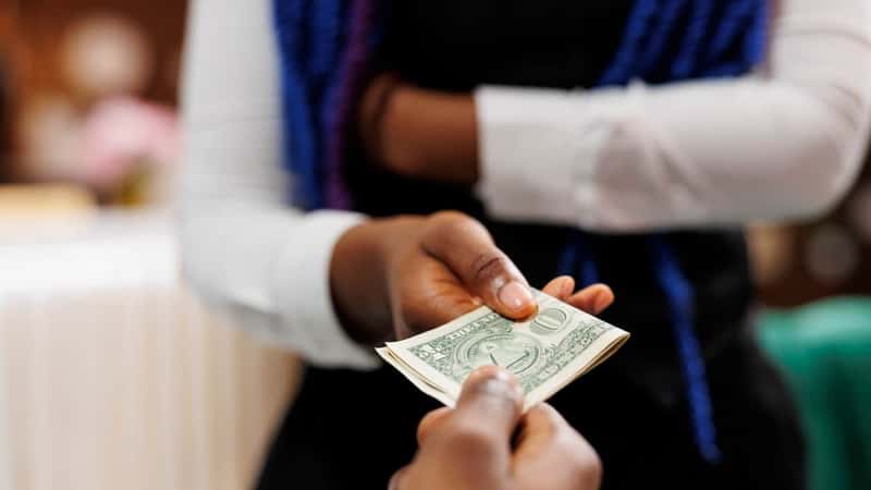 Close up of hotel employee wearing uniform holding money cash taking payment from customer while working in hospitality industry, selective focus.