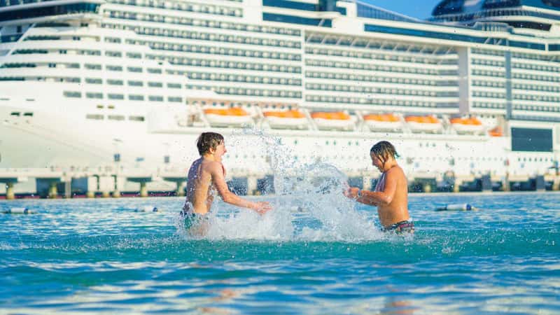 A view of two boys children splashing, playing in the water, in the background the cruise ship, Sir Bani Yas, United Arab Emirates