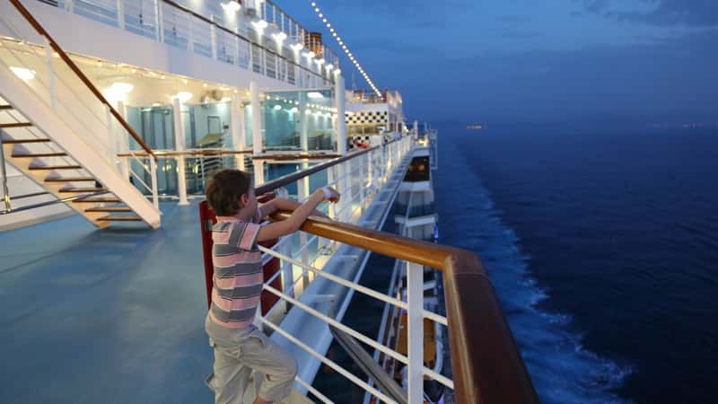 little boy wearing shorts and striped shirt standing on deck of a ship and looking away