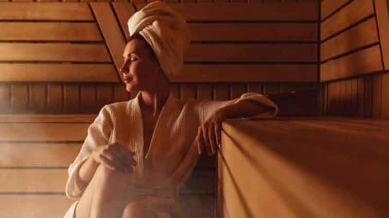 Young woman relaxing and sweating in hot sauna wrapped in towel. Girl In Sauna.