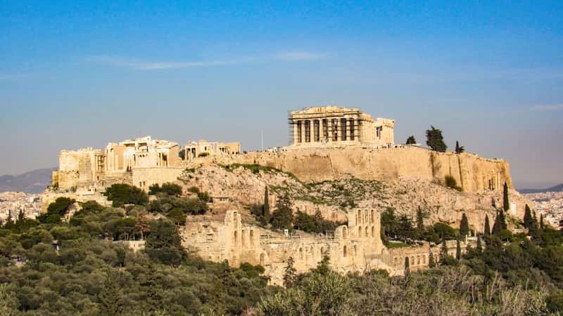 A photograph depicting The Parthenon Temple against a sunny summer day with a clear blue sky. The image showcases the architectural features of The Parthenon, an iconic structure atop the Acropolis mountain in Athens, Europe. 