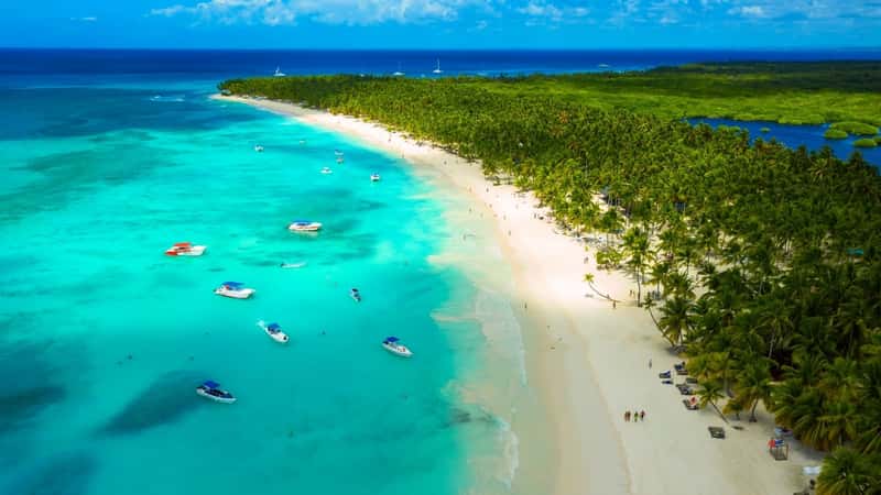 A beautiful Caribbean beach is depicted in the image, showcasing an aerial view of a tropical idyllic summer landscape. The beach features white sand along the sea coast, with clear blue waters stretching out to the horizon.