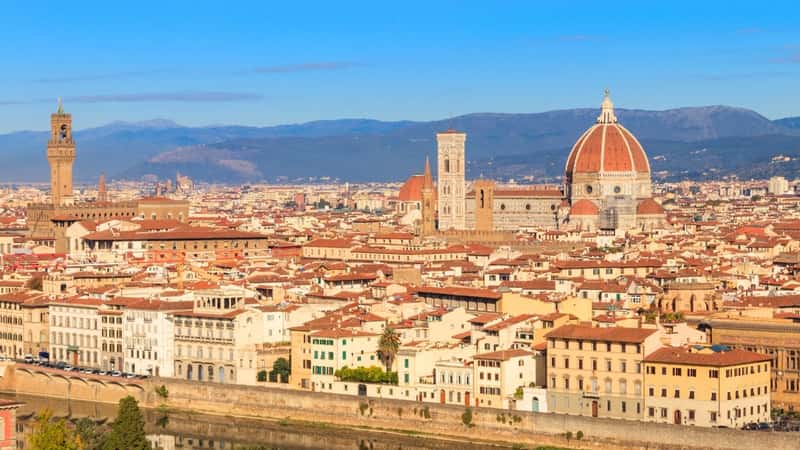 A panoramic photograph capturing the cityscape of Florence from Michelangelo Hill in Tuscany, Italy. The image offers a wide view of the urban layout, highlighting key architectural landmarks and the Tuscan landscape. 