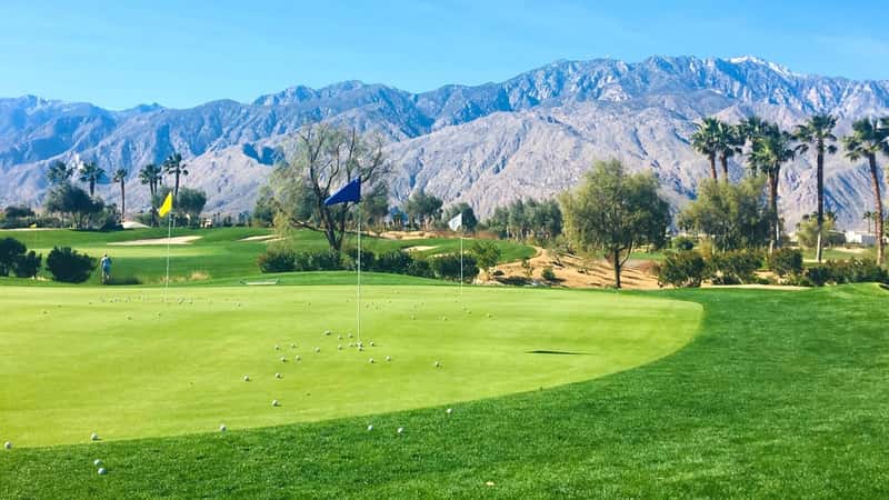 An image capturing the golf course at Indian Canyon Golf Resorts in Palm Springs. The photograph features a well-maintained golf course with lush greenery, framed by a backdrop of distant mountains under a clear sky.