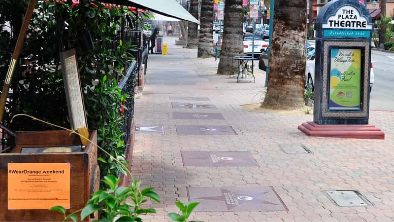 A city street view featuring the Palm Springs Walk of Stars. The image showcases square tiles embedded in the sidewalk, each adorned with stars and signatures.