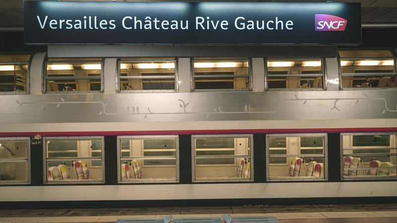 The image depicts a train passenger platform at Versailles-Château-Rive Gauche station in Versailles, France. A regional train is visible on the platform, and notably, there are no commuters present in the scene.