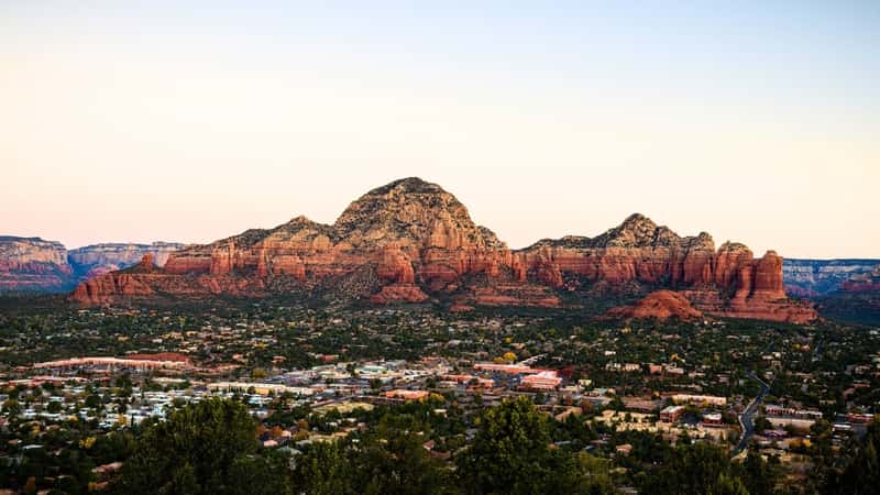 A photograph capturing Capitol Butte and Coffee Pot Rock formation, as viewed from Airport Mesa overlooking the town of Sedona, Arizona, USA. The image depicts the prominent rock formations against the desert landscape.