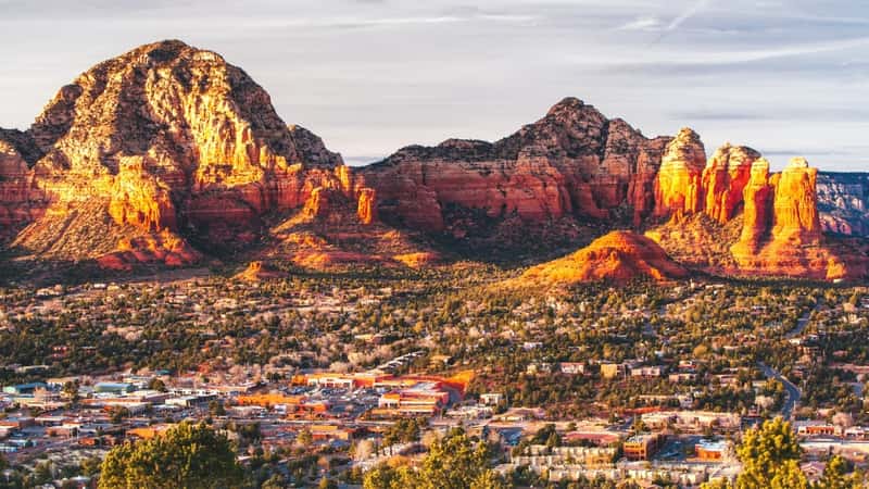  A sunset view from Airport Mesa in Sedona, Arizona, showcasing the scenic beauty of the desert landscape. The image captures the warm hues of the setting sun casting a golden glow over the rugged terrain and red rock formations characteristic of the region. 