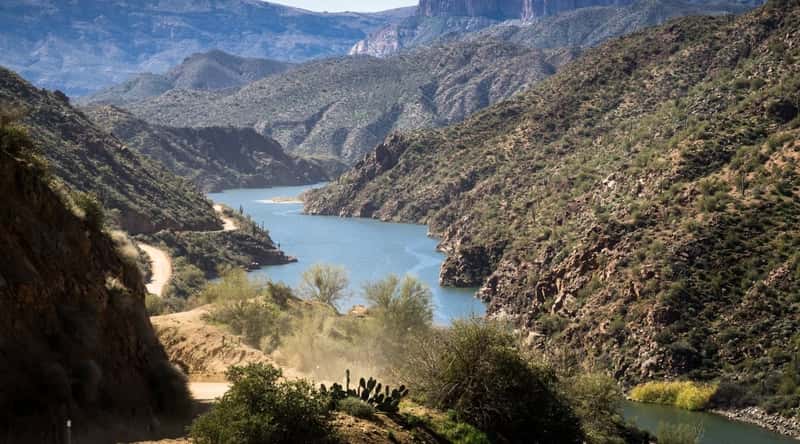 A photograph showcasing Apache Lake in Arizona. The image depicts the lake's clear waters surrounded by desert terrain. Cliffs and mesas frame the lake, contributing to its visual appeal. 
