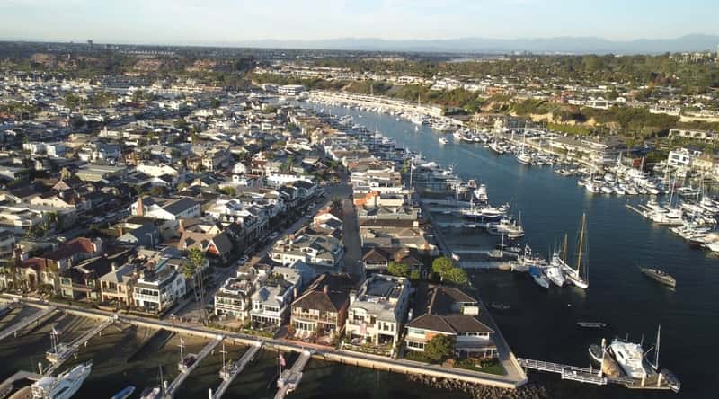 An aerial view capturing Balboa Island and Newport Harbor in Newport Beach, California. The image provides a comprehensive perspective of the coastal landscape, featuring the island and harbor surrounded by water.