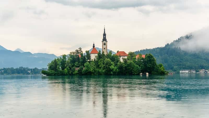 A photograph featuring Beautiful Lake Bled in Slovenia. The image captures the serene beauty of the lake and its surroundings. The calm waters reflect the picturesque landscape of the Bled region.