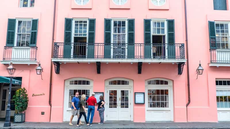 A couple stops to read the menu at Brennan's restaurant in New Orleans, Louisiana. This historic restaurant in the French Quarter features a pink facade with elegant green shutters.