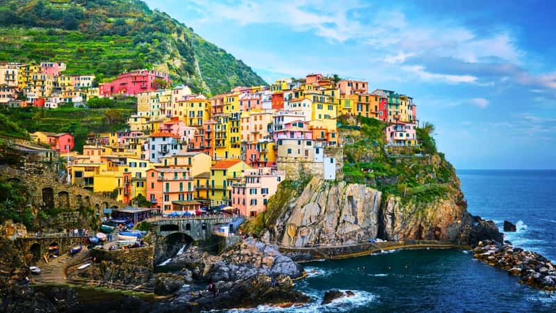 The image depicts Cinque Terre, a UNESCO World Heritage Site located in Liguria, Italy. The houses in Cinque Terre are brightly painted in various colors, creating a vibrant and picturesque scene against the hillside.
