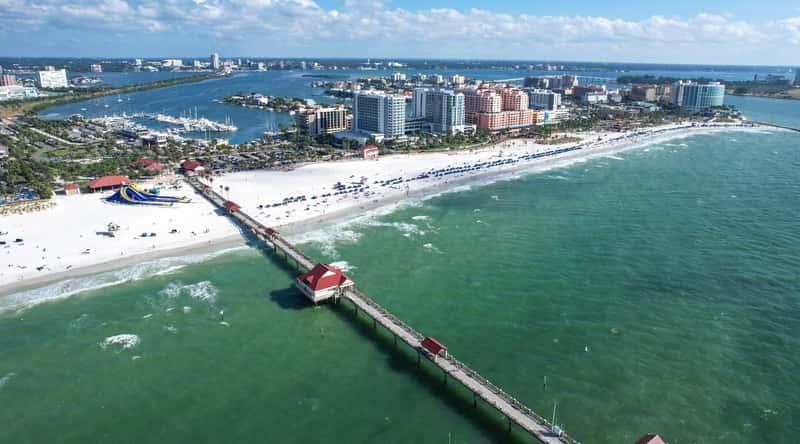 Clearwater Beach in Florida is a stunning white sand beach with crystal-clear waters. View from above, on a long white beach, a beautiful long pier with restaurants. The beach is surrounded by restaurants, shops and other attractions.