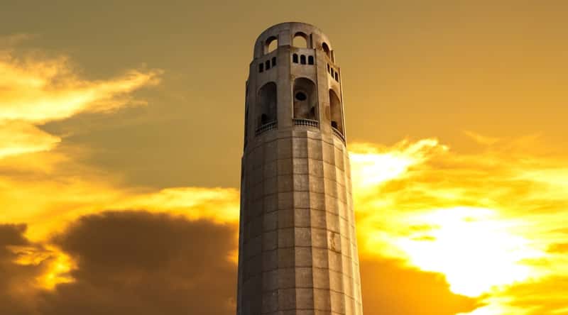 Alcatraz's infamous lookout tower, the Coit Tower, standing tall at sunset with a bright cloudy sky in the background.