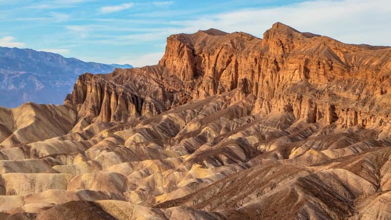 The image depicts Zabriskie Point, a prominent viewpoint in Death Valley National Park. The viewpoint offers a panoramic vista of the eroded badlands landscape, showcasing intricate geological formations and vibrant colors.