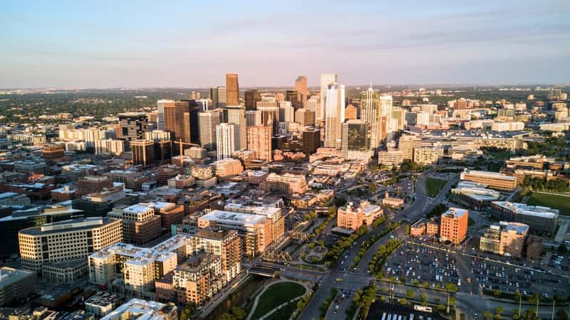 The aerial drone photo captures the cityscape of Denver, Colorado, during sunset. The scene features a mix of skyscrapers and low-rise buildings, showcasing the diverse architecture of the city.