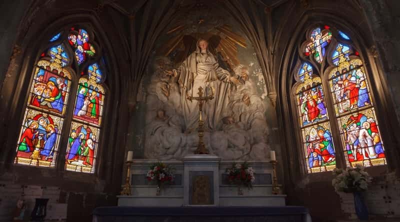 Interior of the Eglise Saint-Aignan in Orleans France illustrating the centerpiece statue and artwork with stained glass windows on each side.