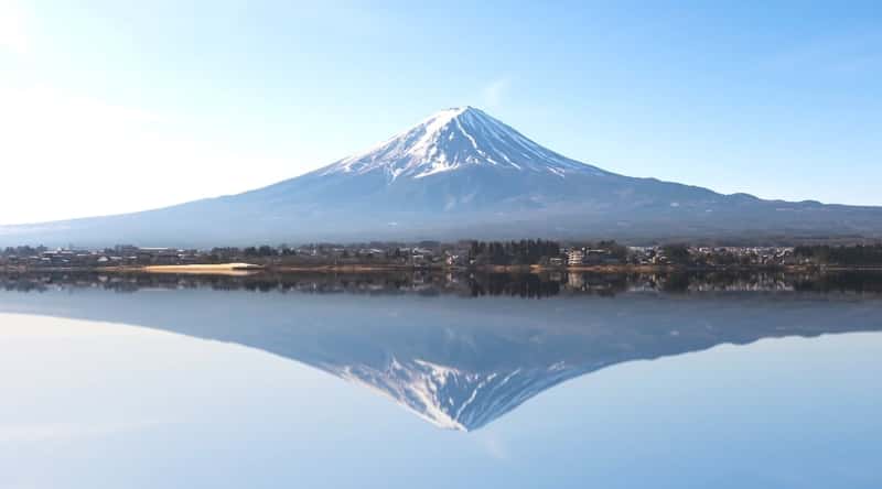 A photograph capturing Mount Fuji, or Fujisan, in its natural setting. The image showcases the iconic conical shape of the mountain, framed against a clear sky.The scene offers a straightforward representation of Mount Fuji, highlighting its distinctive silhouette and geographical prominence.