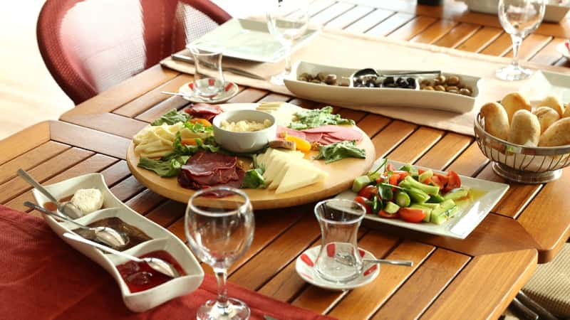 A photograph capturing the interior of Garage-East in Gilbert, Arizona. The image features a table set with snacks, including sliced cheese, sausage, jamón, olives, sauces, and a plate of salad. 