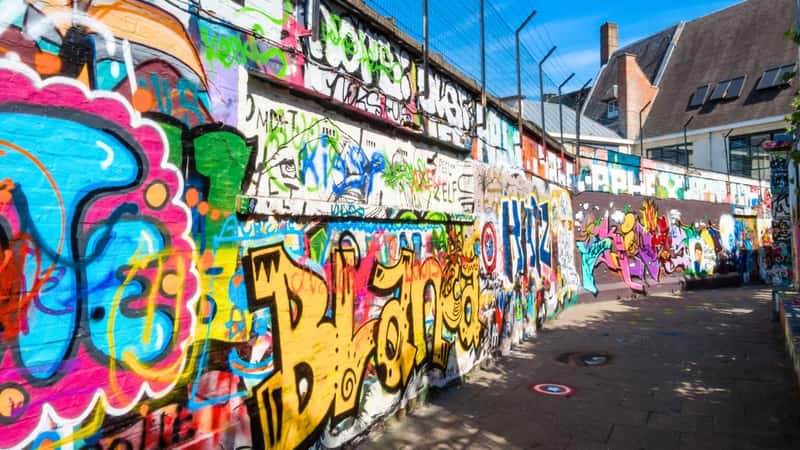 The image captures a scene from Graffiti Street (Werregarenstraat) in Ghent, Belgium. The street is known for its vibrant graffiti art, which covers the walls and surfaces of buildings along the thoroughfare. The graffiti displays a variety of styles, colors, and themes, showcasing the artistic diversity found in this area.