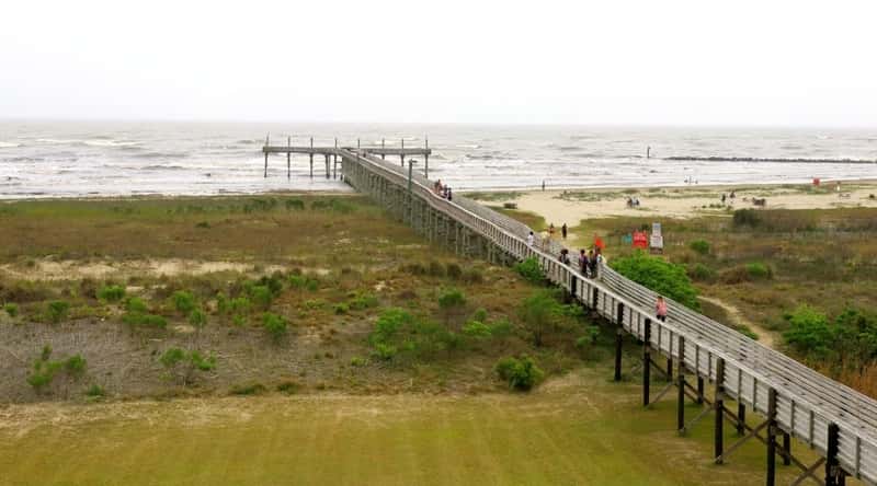 Grand Isle Beach is a long, narrow public beach located on Grand Isle, a barrier island off the coast of Louisiana, USA. The beach is known for its soft white sand and clear blue-green water and is a popular swimming spot. Aerial view of a long pier with people walking along it.