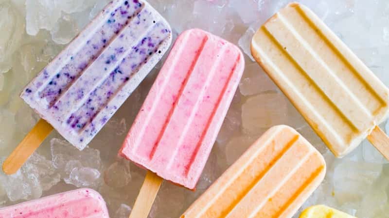 The image features several colored popsicle ice creams lying on a bed of ice, presenting a refreshing and summery scene. The popsicles showcase vibrant colors.