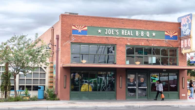 A photograph depicting Joe's Real BBQ, featuring a red brick building with a prominent sign on a green background reading 'Joe's Real BBQ'. 