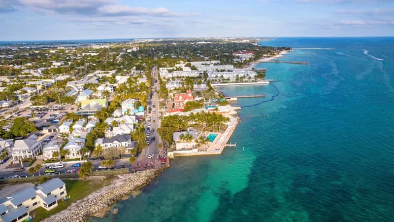 The image showcases a beautiful aerial view of Key West, Florida, capturing both its magnificent beach and the town. The beach is highlighted by its sandy shores and turquoise waters, typical of the region's coastal charm.