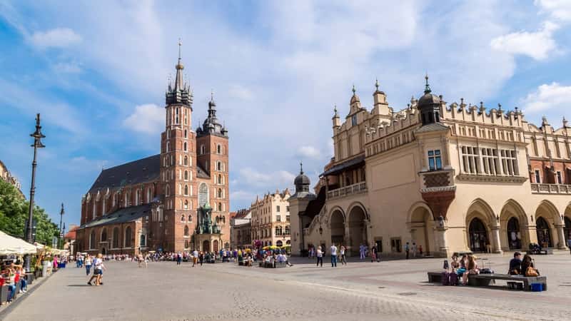 A photograph capturing St. Mary's Church in the historical part of Krakow. The image depicts the church against the backdrop of Krakow during a summer day. The architectural features of St. Mary's Church are observable, showcasing its historical significance. The surroundings include typical elements of the city's urban landscape.