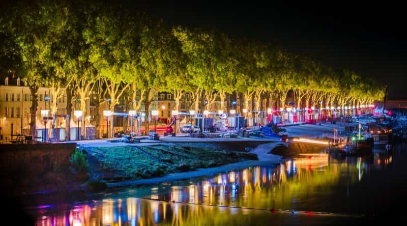 La Paillote on the banks of the Loire River in Orleans France, lit up at night with the lights reflecting off the river.