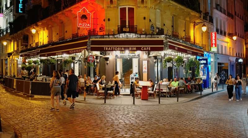 The Latin Quarter is a historic and vibrant neighborhood known for its narrow, winding streets. The interior of the Latin Quarter is characterized by its charming cobblestone streets, lined with cafes, bookshops, and art galleries. Many people sit in cafes and stroll along the streets.