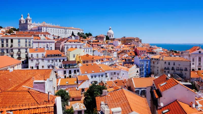 The image features a top view of Lisbon, Portugal, specifically showcasing the Alfama district with its characteristic brown roofs. The aerial perspective offers a comprehensive view of the city's architecture, highlighting the densely packed buildings and narrow streets typical of the Alfama area.