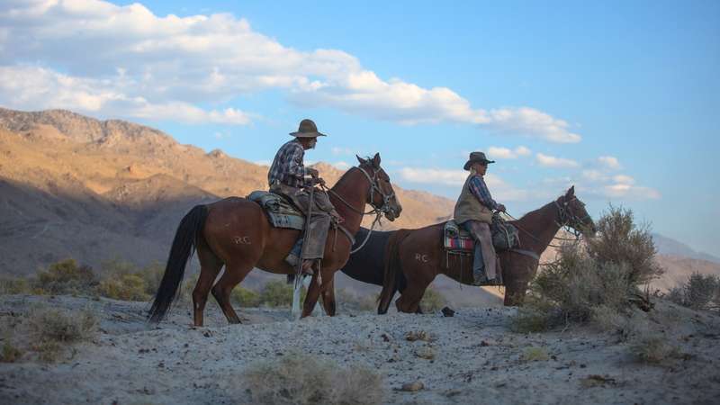  A photograph depicting two men riding horses in a dry, arid landscape.