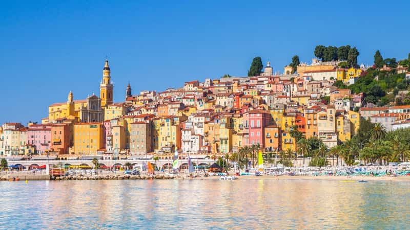 The image depicts the colorful buildings in the medieval town of Menton, situated in the French Riviera along the Mediterranean coast of France. The roofs of the buildings are uniformly brown in color, contributing to the traditional architectural style of the area.