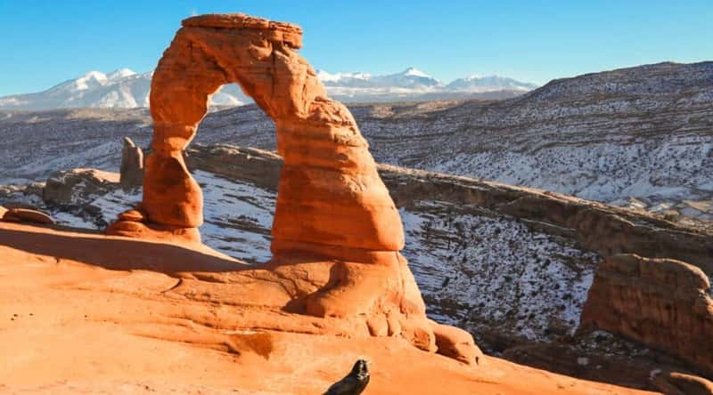 The photograph captures the 52-foot-tall Delicate Arch, a free-standing natural rock arch located in Arches National Park. This well-known natural landmark stands prominently against the backdrop of the La Sal mountain range. The image provides a clear representation of the arch's delicate and distinct form, showcasing its natural features and geographical context.