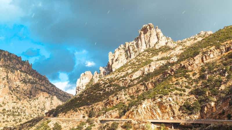 Mount Lemmon in Tucson, Arizona, under a sky filled with gray clouds. The mountain appears rugged and rocky, typical of the desert landscape in the region. Its color scheme includes earthy tones such as browns and grays, accentuated by patches of vegetation where possible. 