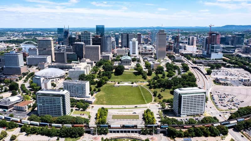 The image depicts a super high, wide, elevated view of the downtown Nashville skyline in Tennessee, USA. The perspective offers a comprehensive view of the cityscape from an aerial vantage point. The skyline features a mix of modern skyscrapers and historic buildings.