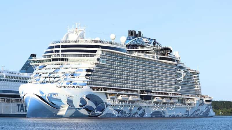 The image features the Norwegian Prima, a Prima Class cruise ship. It is a large vessel adorned with designs of blue waves, and prominently displays the inscription "Norwegian Prima" on its hull.