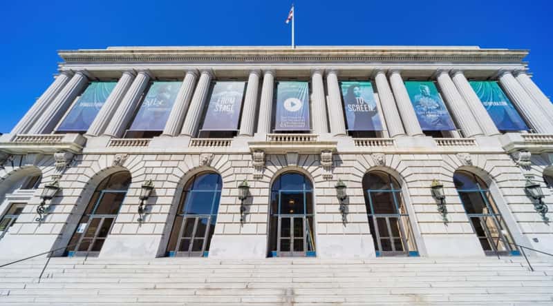 Opera House in San Francisco California. The sun is hitting the building and the steps, with images in some of the windows.