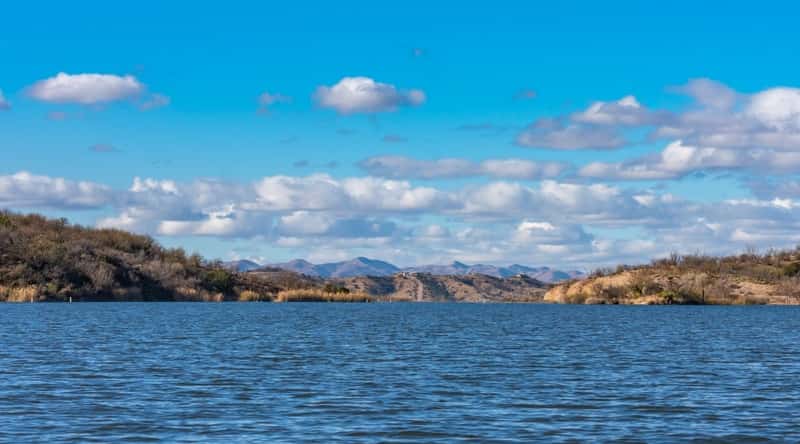 A photograph depicting Patagonia Lake in Arizona. The image lake's scenic setting, framed by desert hills. The shoreline features modest greenery, providing a subtle contrast to the arid surroundings. 