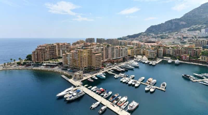 Port de Fontvieille in Monaco. The image showcases the marina with a collection of luxurious yachts and sailboats, set against the azure waters of the Mediterranean Sea. The facades of elegant waterfront buildings surround the port, reflecting a blend of modern architecture and coastal charm.