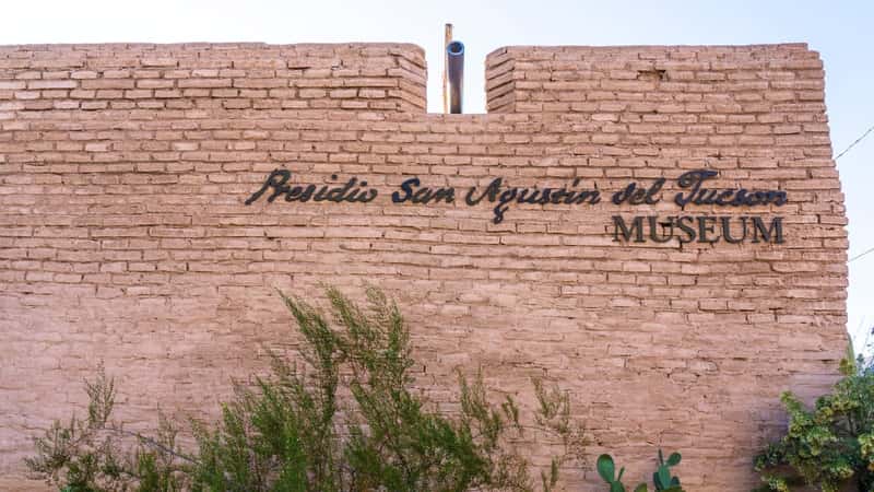 The image depicts the inscription "Presidio San Agustín del Tucson Museum" crafted in brown sienna stonework. 