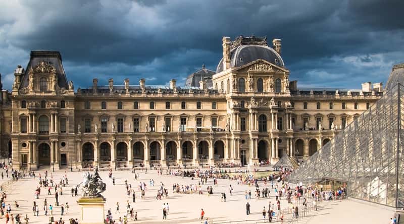 A photograph featuring The Louvre in Paris, France, showcasing the famous glass pyramid and the Richelieu Wing. The Louvre is renowned as the world's largest art museum and stands as one of the most visited historic monuments globally.