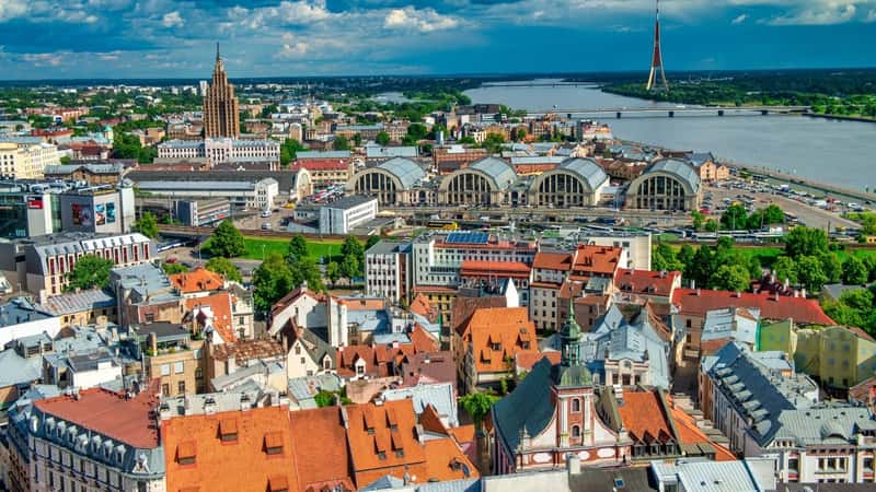 A photograph capturing the Riga skyline on a sunny afternoon. The image showcases the cityscape . Prominent buildings and architectural structures contribute to the urban panorama, reflecting the city's distinctive architectural style.