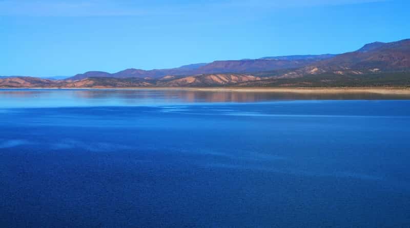 Photograph showcasing the scenic beauty of Roosevelt Lake in Arizona. The image captures the expansive reservoir nestled amidst the rugged desert landscape. The clear blue waters of the lake reflect the azure sky.