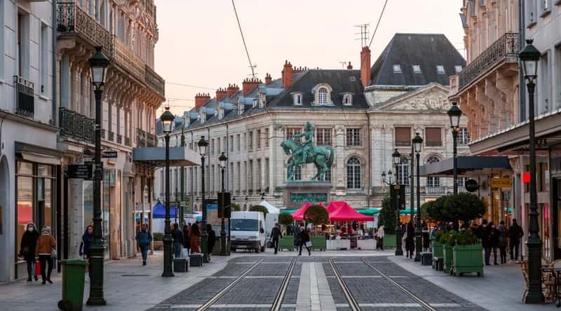 Rue Royale looking down at the Joan of Arc Statue in Place du Martroi, Orleans, France, with tourists walking along the sidewalks.