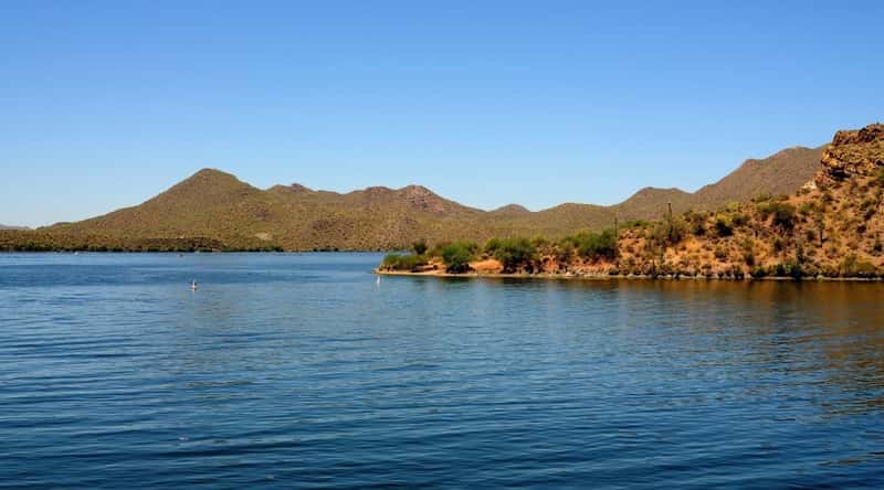 Saguaro Lake in Arizona. The image showcases the tranquil waters framed by the rugged desert landscape. The clear blue sky reflects on the calm surface of the lake, creating a picturesque panorama. 