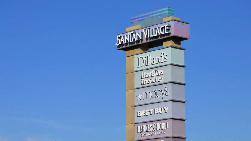 A photograph depicting a tall sign displaying the inscription 'SanTan Village' along with a list of stores including Dillard's, Macy's, Best Buy, and others. 
